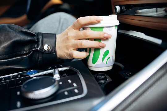 Woman's hand holding a disposable coffee cup while sitting in a car, enjoying a daily commute and relaxing moment