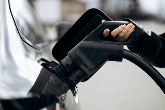 Woman's hand connecting ev charger to an electric vehicle, promoting sustainable transportation and green energy