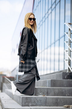 Woman in a leather jacket and wide-leg trousers walking up concrete steps, smiling, reflecting urban fashion and lifestyle