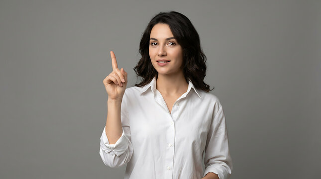 A confident young woman in a white shirt raising her index finger to signal an idea or important point, against a neutral gray background