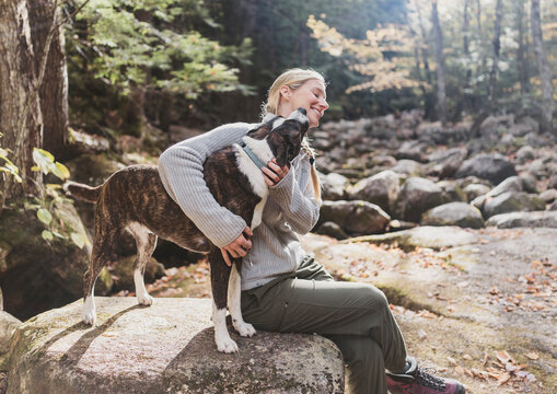 Happy young woman hugging her brindle dog in the forest