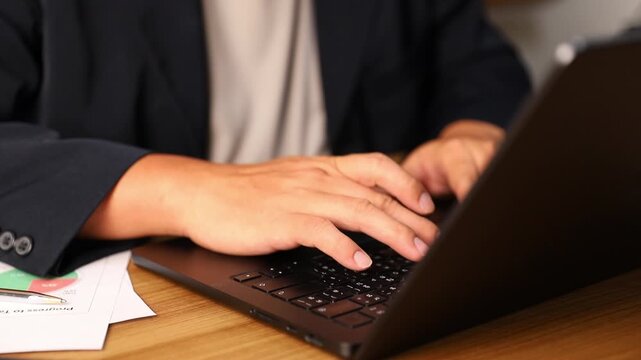 Close up of hands typing on laptop keyboard at wooden desk in soft natural light, modern workspace concept showing productivity, online communication, working remote and digital technology environment
