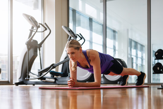 Athletic woman doing plank exercise on a fitness mat at gym