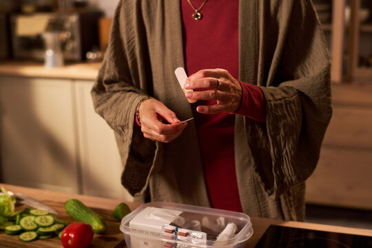 Middle aged Caucasian woman applying adhesive bandage on finger after kitchen injury during meal preparation. Ideal for home first aid and healthcare campaign