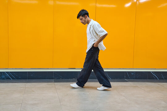 Young man walking against vivid orange wall