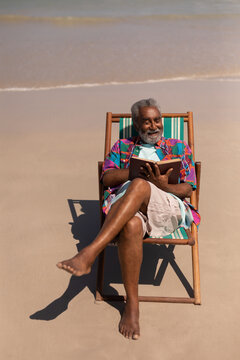 Senior man relaxing on sun lounger and reading a book on beach