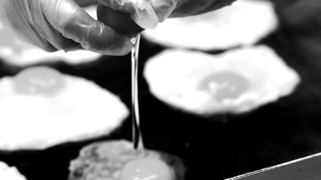 A cook carefully fries several sunny side up eggs on a hot black griddle
