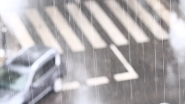 Lluvia con ambiente difuminado y borroso en calle de ciudad con gotas de agua y charcos en tormenta y chubasco con coche y paso de peatones