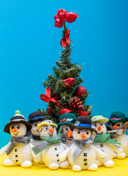 snowman crocheted from yarn, placed on a colorful background next to a Christmas tree