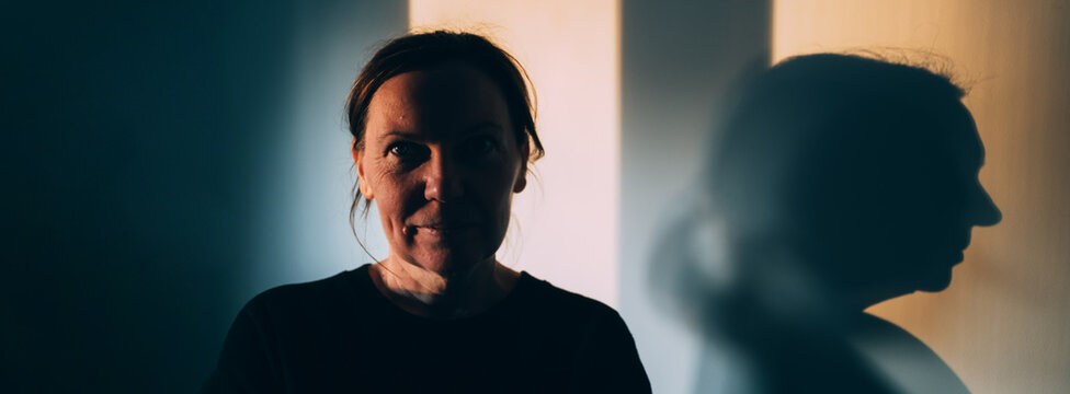 Woman and her large silhouette shadow on a wall in warm and cool tones, concept of duality, identity, hidden self and introspection, with copy space