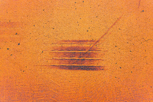 Dark horizontal tire skid marks on a bright orange painted road surface, with cracked paint, fine gravel grain and a thin diagonal scratch across the textured background.