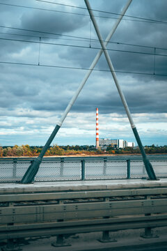 Industrial power plant with a red and white striped smokestack viewed from a bridge beneath dramatic cloudy skies. Energy production, industrial infrastructure and environmental themes.