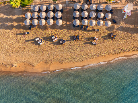 Aerial top view of a beach in Greece with sunbed and sunshade at sunset