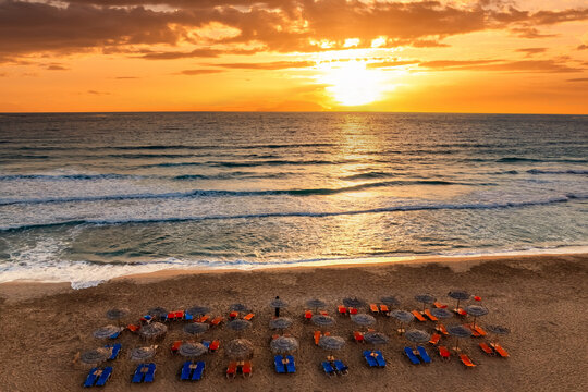 Aerial top view of a beach in Greece with sunbed and sunshade at sunset