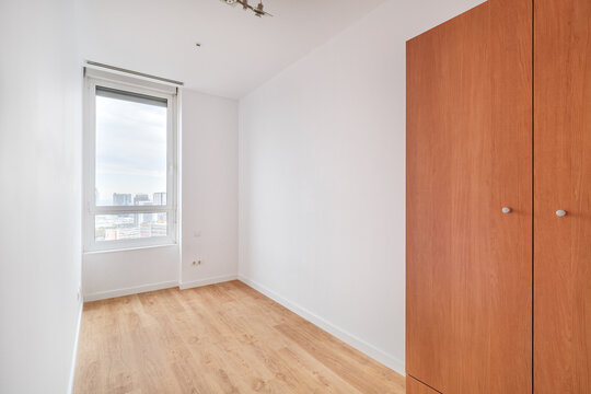 Empty bright interior room with wooden floor, large window, light walls, and built-in wardrobe, filled with natural daylight for clean minimal home design, with room, empty, bright, interior detail