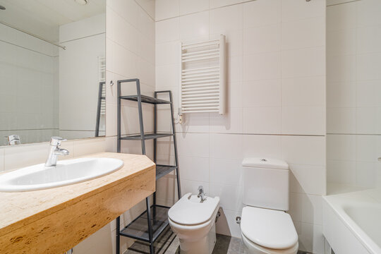 Modern bright bathroom with wooden countertop sink, white toilet, bidet, and built-in bathtub in light tiled interior with clean minimalist residential styling, with bathroom, modern, bright, wooden