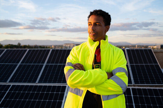 Man in high-visibility jacket standing by solar panels at sunset