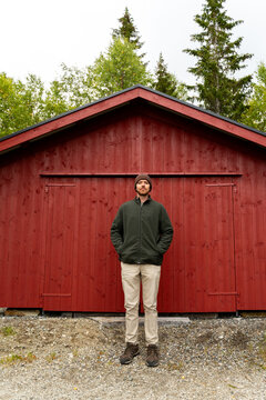 Man standing outside red wooden shed in Norway outdoors