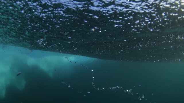 White bubbles churn under breaking ocean wave, filling blue water, turbulence at midday