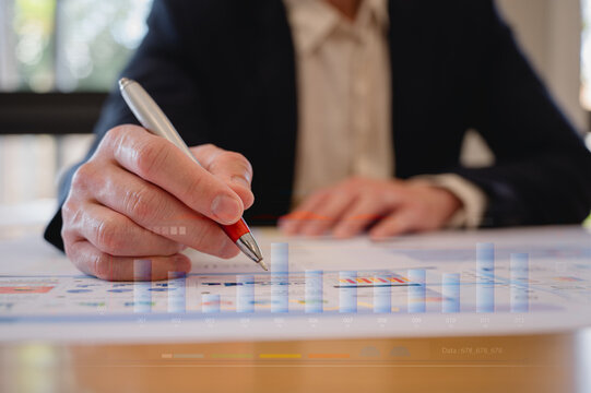 Businessman using pen analysing data charts on table in modern office in Business planning and investment financial data analytics graph Financial management technology concept.