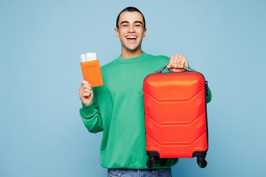 Traveler surprised fun man wear green casual clothes hold bag passport ticket isolated on plain blue background. Tourist travel abroad in free spare time rest getaway. Air flight trip journey concept.