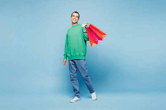 Full body side view young man wear green casual clothes hold in hand paper package bags after shopping walk go look aside isolated on plain pastel blue background. Black Friday sale buy day concept
