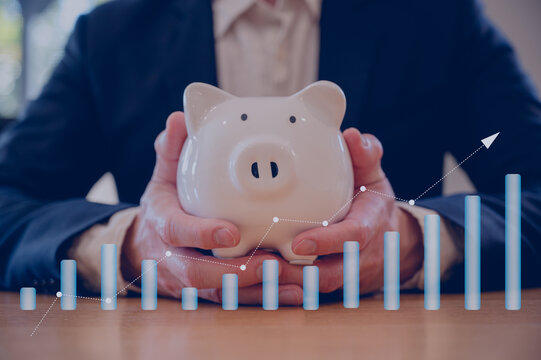 Businessman hand holding piggy bank on wood table in business finance and saving money investment concept.