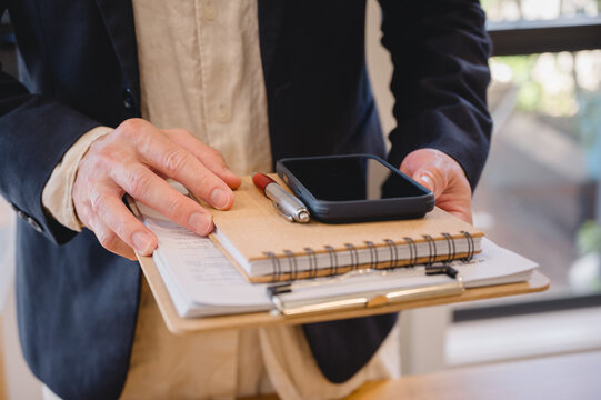Business professional holding a clipboard with documents, notebook, smartphone and pen, representing office administration, business planning, productivity, communication and organization.