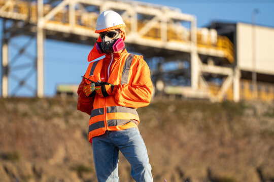Industrial worker in protective gear checking a handheld device at an outdoor industrial site