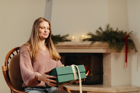 Woman holding christmas gift by fireplace enjoying holidays