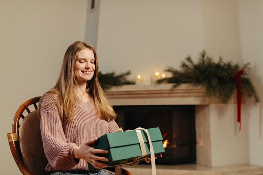 Happy woman holding christmas gift by cozy fireplace