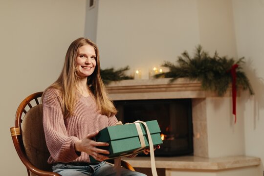 Young woman holding christmas gift by fireplace