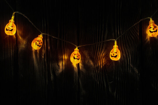 Glowing Halloween pumpkin lights hang on a dark rustic wooden wall