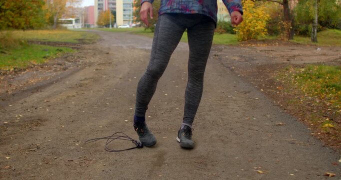 Teen student in outdoor autumn setting skips rope on dirt path near apartment blocks during Czech Republic school graduation celebration, wearing patterned top