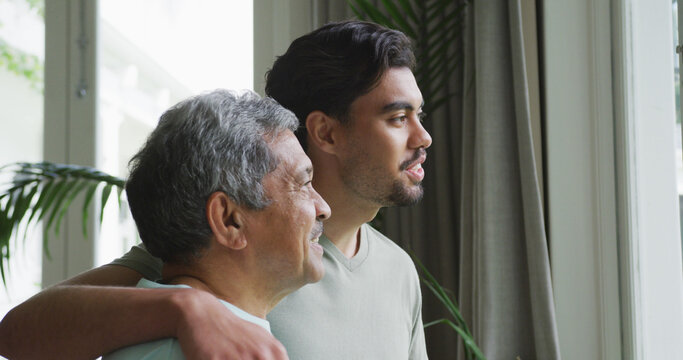 man smiling and keeping hand on shoulders of thoughtful father looking away at home