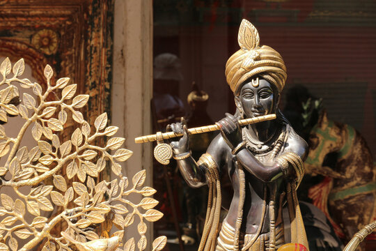 A horizontal view of a bronze Lord Krishna statue playing flute displayed next to a brass decorative tree.