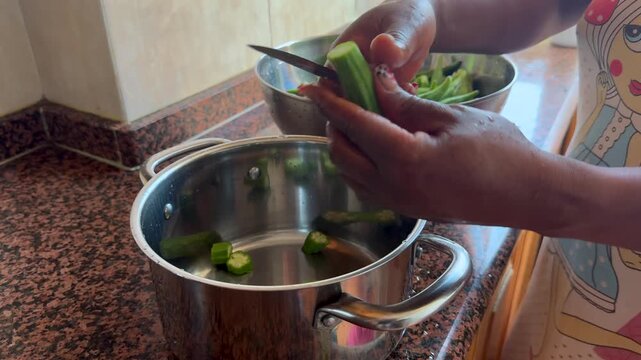 closeup view of the hands of a young black woman chopping okro into pieces in a bowl inside a kitchen