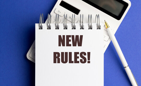 New rules text on a spiral notebook with calculator and pen on blue background, regulation change and business compliance concept