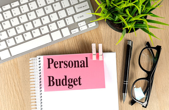 Personal budget notebook with keyboard, pen, glasses and plant on a wooden desk, home finance planning concept