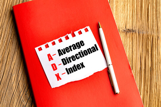 Average directional index trading analysis concept with text on torn paper, red notebook and white pen on a wooden desk
