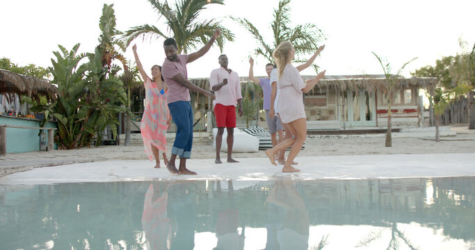 Happy diverse group of friends dancing with sparklers at swimming pool