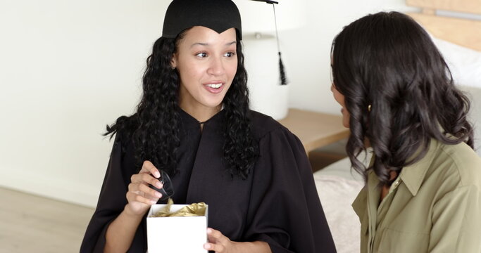Graduate in cap and gown smiling while reading card with supportive friend nearby