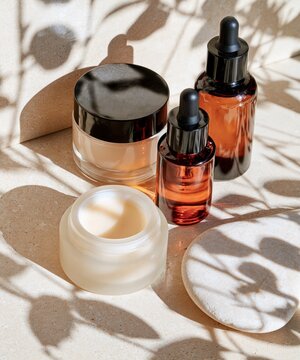 Several skincare products are arranged on a textured surface with dappled sunlight and plant shadows.