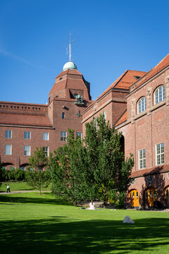 Historic red-brick institutional building and leafy courtyard beneath a clear Stockholm sky