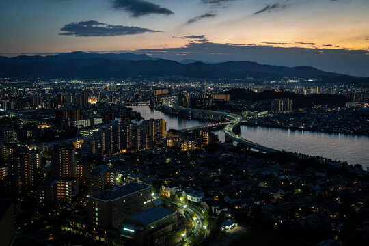Panoramic view of Fukuoka city lights beside a winding river and mountain ridge at sunset