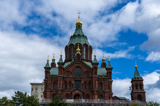 Red brick Orthodox cathedral with green domes rises beneath a dramatic Helsinki sky