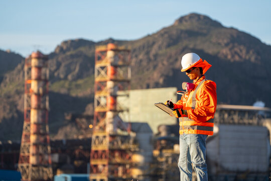 Industrial latino safety engineer wearing protective gear, recording inspection notes at a refinery