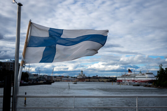 Large Finnish flag waving above Helsinki harbor with a passenger ship under cloudy skies