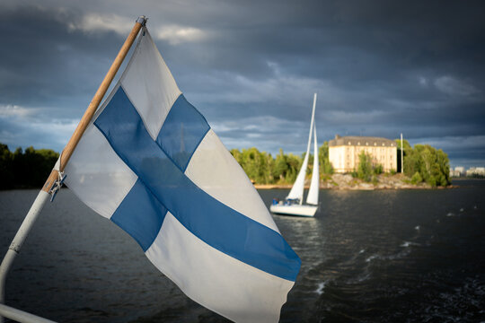Close view of the Finnish flag with sailboats crossing Helsinki harbor under dramatic storm clouds