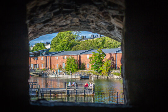 Helsinki canal and red brick waterfront framed through a dark stone archway in summer